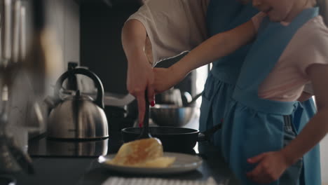 mother-is-teaching-her-little-daughter-to-fry-pancakes-woman-and-child-are-standing-near-stove